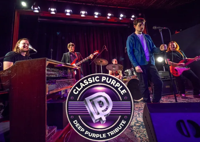Five band members smiling onstage with their instruments, band name in logo