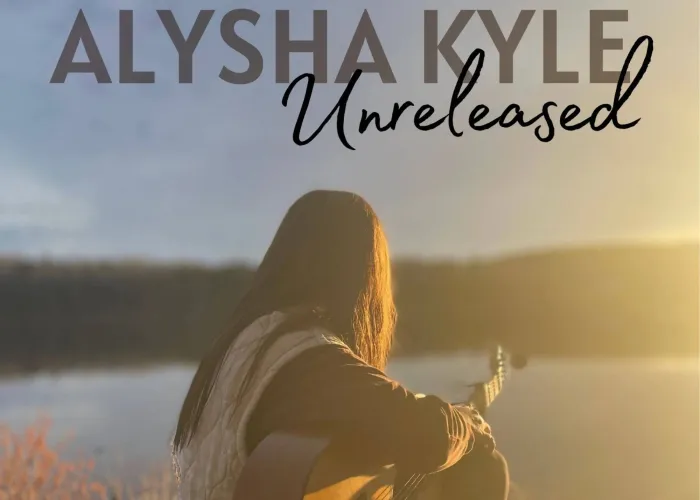 Alysha Kyle facing away holding guitar, lake and trees in background