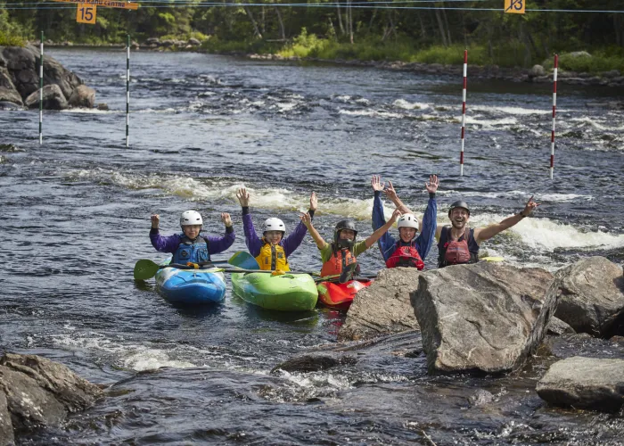 Five Kayakers lined up in river behind boulders with hands raised in air